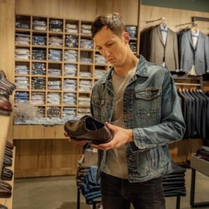 A young man inspects leather shoes in a stylish boutique's menswear section.