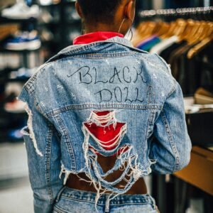 Back view of a woman wearing a ripped jean jacket with 'Black Doll' text in a fashion store.