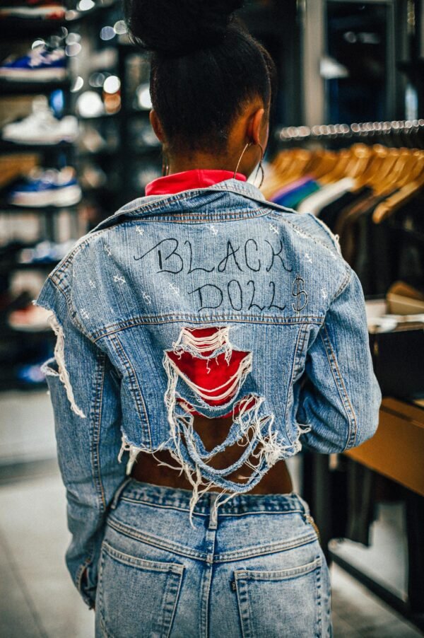 Back view of a woman wearing a ripped jean jacket with 'Black Doll' text in a fashion store.